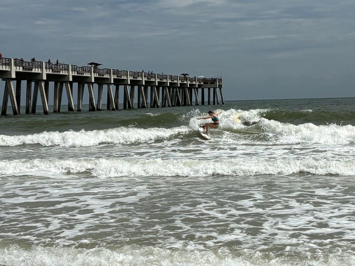 A surfer carving a wave beside the Jacksonville Beach Pier at the Wavemasters Surf Contest
